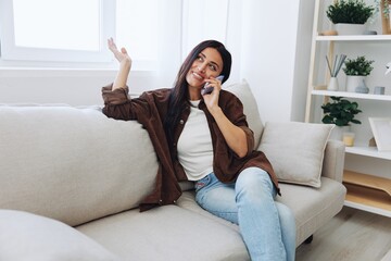 Woman blogger with phone lying at home and talking on the phone on sofa with laptop and working freelancer online, smiling with teeth