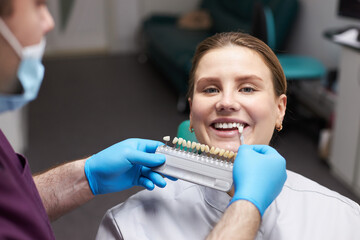 Close-up female patient looking at camera while orthodontist, choosing the shade of dental veneers