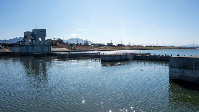 春の遠賀川水門と静かな水面の川の流れ、遠くに福智山を見る、The sluice gate of the Onga River and the quiet flow of the river, with a view of Mt. Fukuchi in the distance