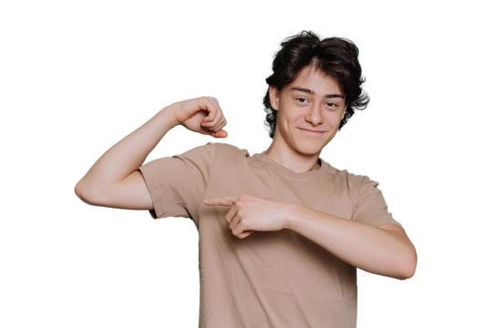 Handsome caucasian schoolboy in beige t-shirt bending arm demonstrates biceps pointing at it by index finger of another hand stands against transparent background. Cheerful Italian teen shows strength - Powered by Adobe