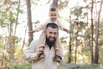 Father's day. Smiling dad holding his toddler son on shoulders look at camera outdoor at nature. Family spend and enjoy time together. Happy fatherhood and childhood, family love, togetherness concept