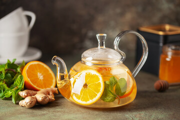 Glass teapot with hot citrus tea from oranges, lemons, apples, ginger and mint. Healthy drink on dark background