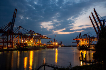 Fototapeta na wymiar Hamburg Hafen Container Terminal mit Hafengiraffen und Frachtschiffen zur blauen Stunde Dämmerung