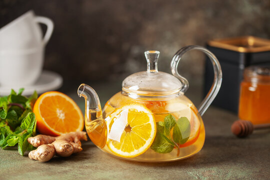 Glass teapot with hot citrus tea from oranges, lemons, apples, ginger and mint. Healthy drink on dark background - Powered by Adobe