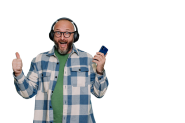 Amazed bald caucasian mid adult beardy man in plaid shirt in headphones gestures thumb up holds phone against transparent background with empty space. Scandinavian male enjoys music.