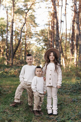Fototapeta premium Portrait of happy adorable kids outdoors. Siblings, two stylish little brothers with their older sister hugging together in autumn park, smiling and looking at camera. Happy childhood concept