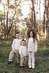 Portrait of happy adorable kids outdoors. Siblings, two stylish little brothers with their older sister hugging together in autumn park, smiling and looking at camera. Happy childhood concept