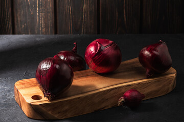 Bulbs of red onion on a wooden cutting board.