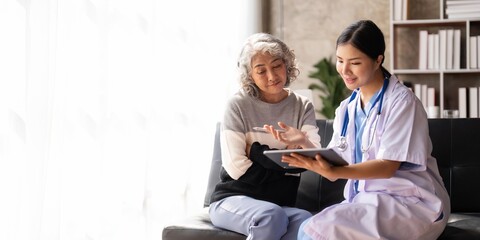 Nurse talking with a nursing home patient about his health. The nurse is making notes on a digital...