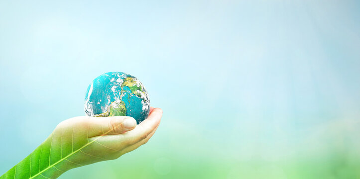Human hands holding earth globe over blurred green nature and blue sky background. Elements of this image furnished by NASA