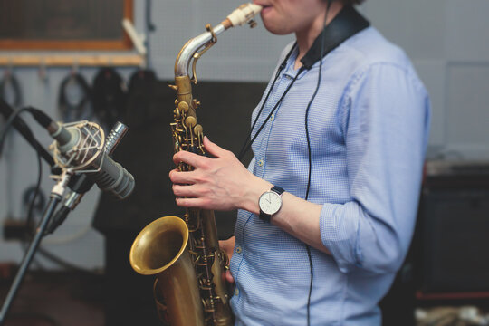 View of a saxophone player in headphones during rehearsal, recording sound for new album song at studio, saxophonist musician in front of microphone with musical band orchestra, music production