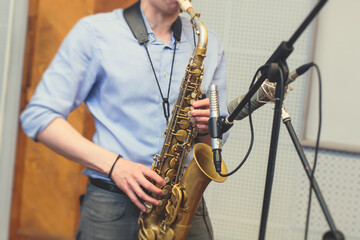 Fototapeta na wymiar View of a saxophone player in headphones during rehearsal, recording sound for new album song at studio, saxophonist musician in front of microphone with musical band orchestra, music production