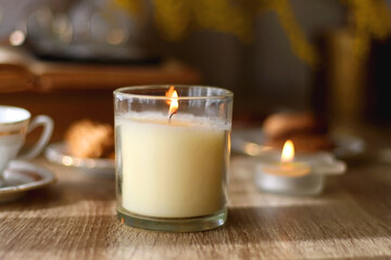 Scented candles, on the table. Selective focus.chocolate, cookies, cup of tea, books, e-reader, glasses and flowers on the table. Hygge at home. Selective focus.