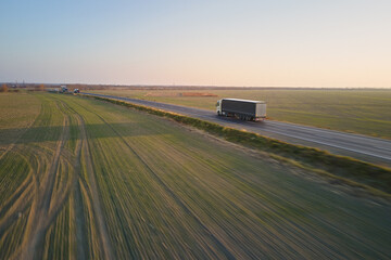 Aerial view of semi-truck with cargo trailer driving on highway hauling goods in evening. Delivery...