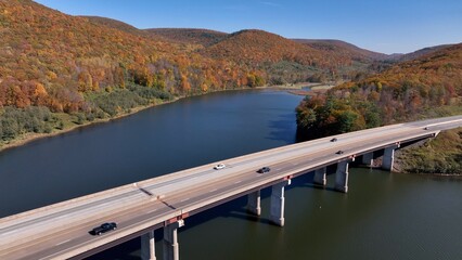 Cars and trucks traveling on highway crossing bridge over Tioga Reservoir in Autumn with Fall Colors