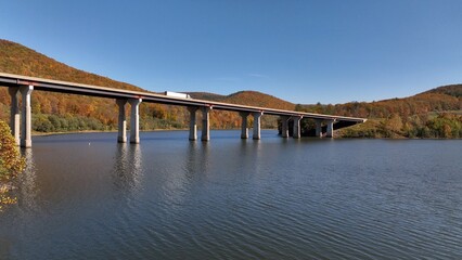 Cars and trucks traveling on highway crossing bridge over Tioga Reservoir in Autumn with Fall Colors