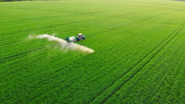 Aerial video of tractor spraying soil and young crop in springtime in field. Tractor spraying pesticides on soy field with sprayer at spring. Nozzle of the tractor sprinklers sprayed.