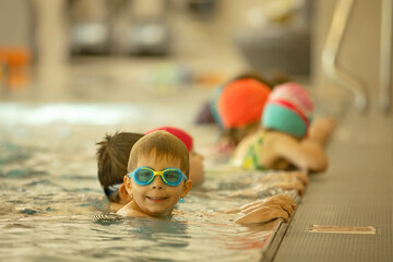 Child, taking swimming lessons in a group of children in indoor pool, enjoying