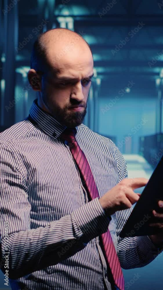 Poster vertical video: data center it engineer standing in server room with rack cabinets, inspecting cloud