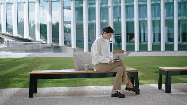 Girl studying online laptop on bench near office. Woman taking remote courses.