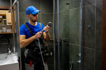 Young handsome plumber in uniform, fixing the shower. Fixing the shower hose and mixer in the...