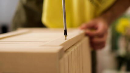 Closeup man hand using manual screwdriver and screwing screw in board. Assembling new wooden furniture.