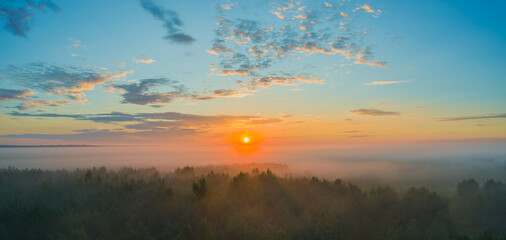Dawn in morning in summer over forest with light fog over tops of trees with beautiful skies and sunshine