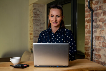 Fototapeta premium Beautiful woman is working on a laptop computer late at night. A young creative manager feels happy, looks at the camera and smiles
