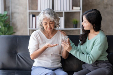 Asian elderly woman taking medicine for her ailments in the living room at home under the close supervision of her daughter.