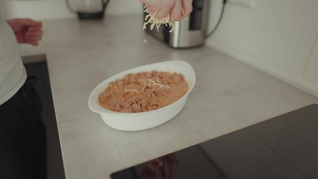 Zeitlupenaufnahme von einem jungen Mann, der K&auml;se &uuml;ber einen Auflauf streut
