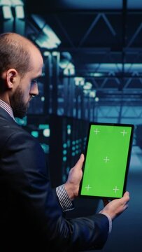 Vertical video: Database admin analyzing greenscreen display on tablet, doing web system check in server room. IT engineer using mockup copyspace display with isolated chroma key. Tripod shot.