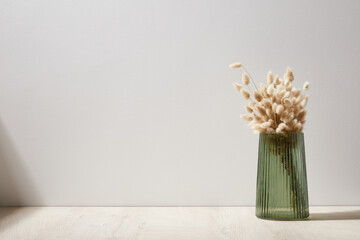 green glass vase with dry flowers stand on a wooden desk, background white wall © ShapeImages