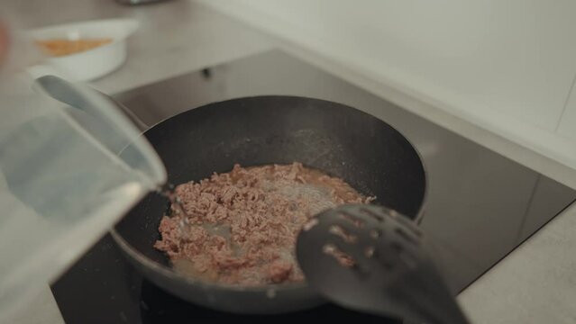 H&uuml;bscher Mann gibt Wasser zu Hackfleisch in eine Induktions Pfanne