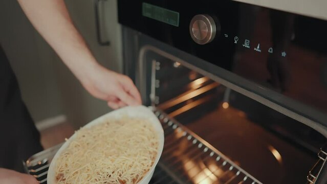 junger Mann schiebt einen Auflauf in den Backofen