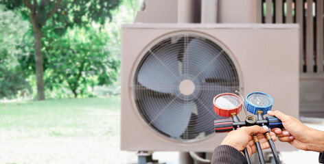 Air repair mechanic using measuring equipment for filling industrial factory air conditioners.	