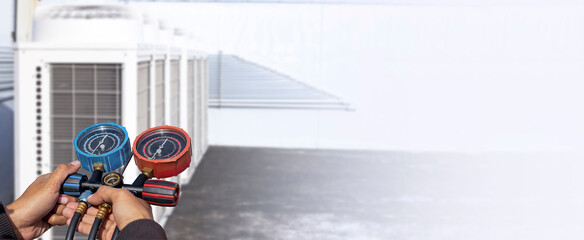 Air repair mechanic using measuring equipment for filling industrial factory air conditioners.	