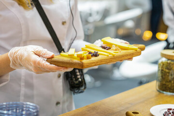 Wooden board with assorted cheeses in hands of promoter girl