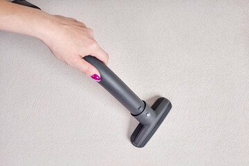 Naklejka premium Close-up of a female hand vacuums the surface of the beige sofa