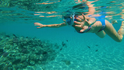 Fototapeta na wymiar in the sea, a girl in a special snorkeling mask swims, examines fish, corrals, the beauty of the underwater world, on a hot summer day, while on vacation.
