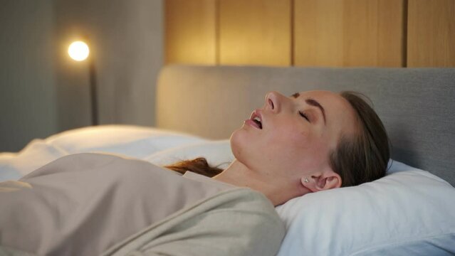 Heterosexual couple in bed, a woman sleeps and scores with her mouth open, while a tired man, irritated by snoring, holds a woman's nose