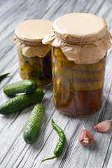 Pickled cucumbers in glass jars and spices and vegetables for preparation of pickles on old wooden background.