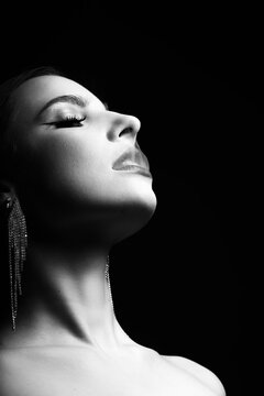 Fashion and make-up concept. Beautiful woman studio portrait with fancy earrings and lipstick blowing white smoke through mouth. Model looking up with partly close eyes. Black and white image