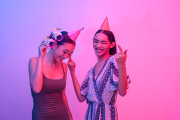 Two happy best friends wearing party hats dancing. A straight and trans woman grooving together at an event. Lit with blue and pink neon colors.