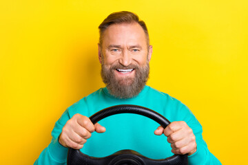 Photo portrait of handsome granddad holding steering wheel toothy smile dressed stylish cyan look isolated on yellow color background