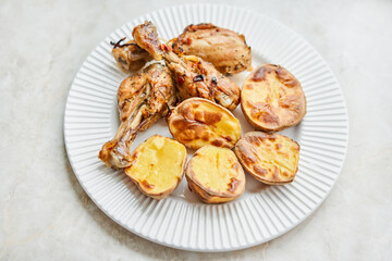 Chicken baked in pieces with potatoes and onion on a white dish. Home cooking. Healthy food, cooked without oil and salt.