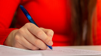 A girl at the table writes with a pen in a notebook. Student studying, taking notes. School and education. Closeup photo