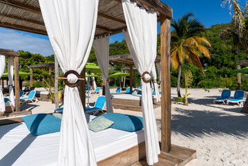 Fototapeta na wymiar Beach cabanas overlooking the Caribbean Sea. Relax in the shade. Beach, sand, umbrellas, loungers, curtains, palm trees, beach beds. Adrenaline Beach, Labadee, Haiti private resort by Royal Caribbean.