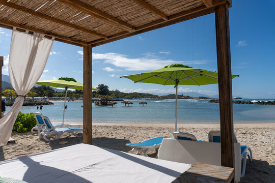 Beach cabanas overlooking the Caribbean Sea. Relax in the shade. Beach, sand, umbrellas, loungers, curtains, palm trees, beach beds. Adrenaline Beach, Labadee, Haiti private resort by Royal Caribbean.