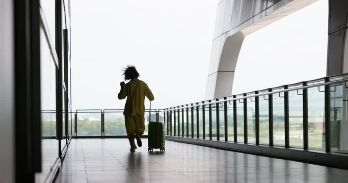 Back of woman traveler who rejoices at opening of borders after covid-19 epidemic. Adventurous woman can finally travel world calmly and freely. Woman dances while hopping through airport with luggage