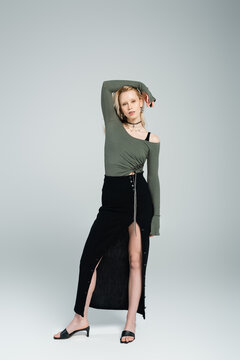 full length of blonde young woman in long sleeve and sexy skirt posing on grey.